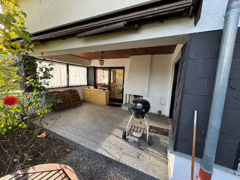 Zwangsversteigerung Einfamilienhaus in Marburg, Bauerbach – Überdachter Terrassenteil mit Außenkamin und Natursteinbelag.