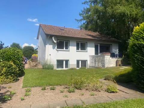 Zwangsversteigerung Einfamilienhaus in Lage – Südliche Gartenansicht des Wohnhauses mit Rasenfläche und Terrasse.
