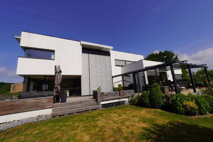 Zwangsversteigerung Zweifamilienhaus in Bergkamen, Overberge – Ostansicht des Gebäudes mit Gartenbereich und überdachter Terrasse.