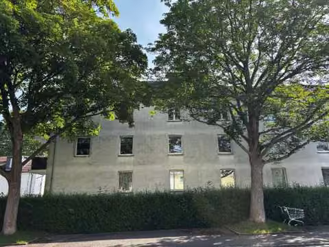 Zwangsversteigerung Eigentumswohnung in Dortmund, Dorstfeld – Westansicht des Gebäudekomplexes mit Grünfläche und Bäumen.